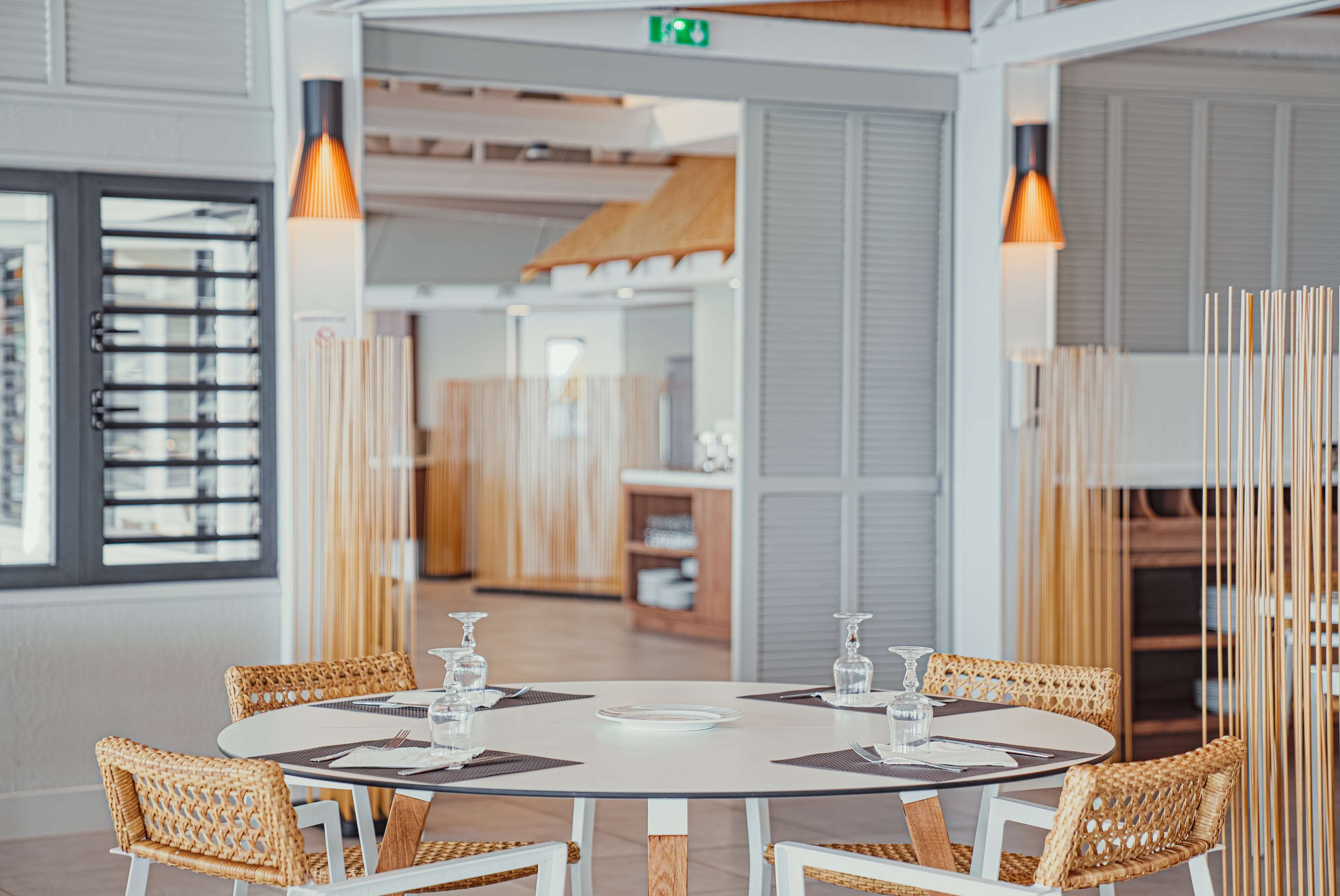A round dining table with white chairs, surrounded by vertical wooden slats, in a modern interior with a view of a cityscape through large windows.