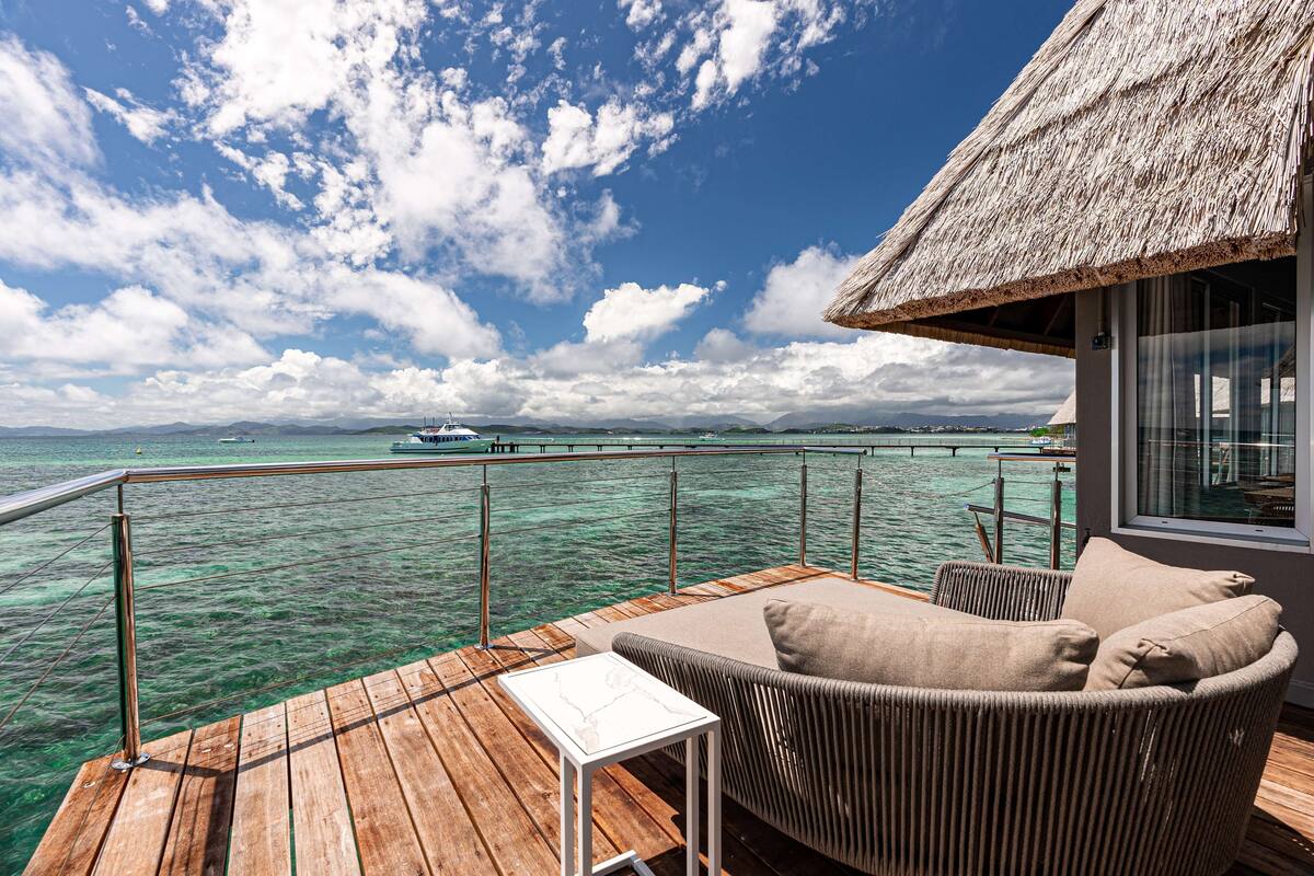 A wooden deck with a thatched-roof structure, a wicker sofa, and a small table.