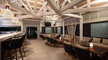 Ruime binnenruimte met een hoge plafond, een bar met krukjes en zithoekjes met banken en stoelen.