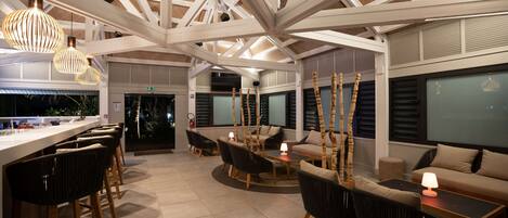A spacious indoor area with a high ceiling, a bar area with stools, and seating arrangements including sofas and chairs.