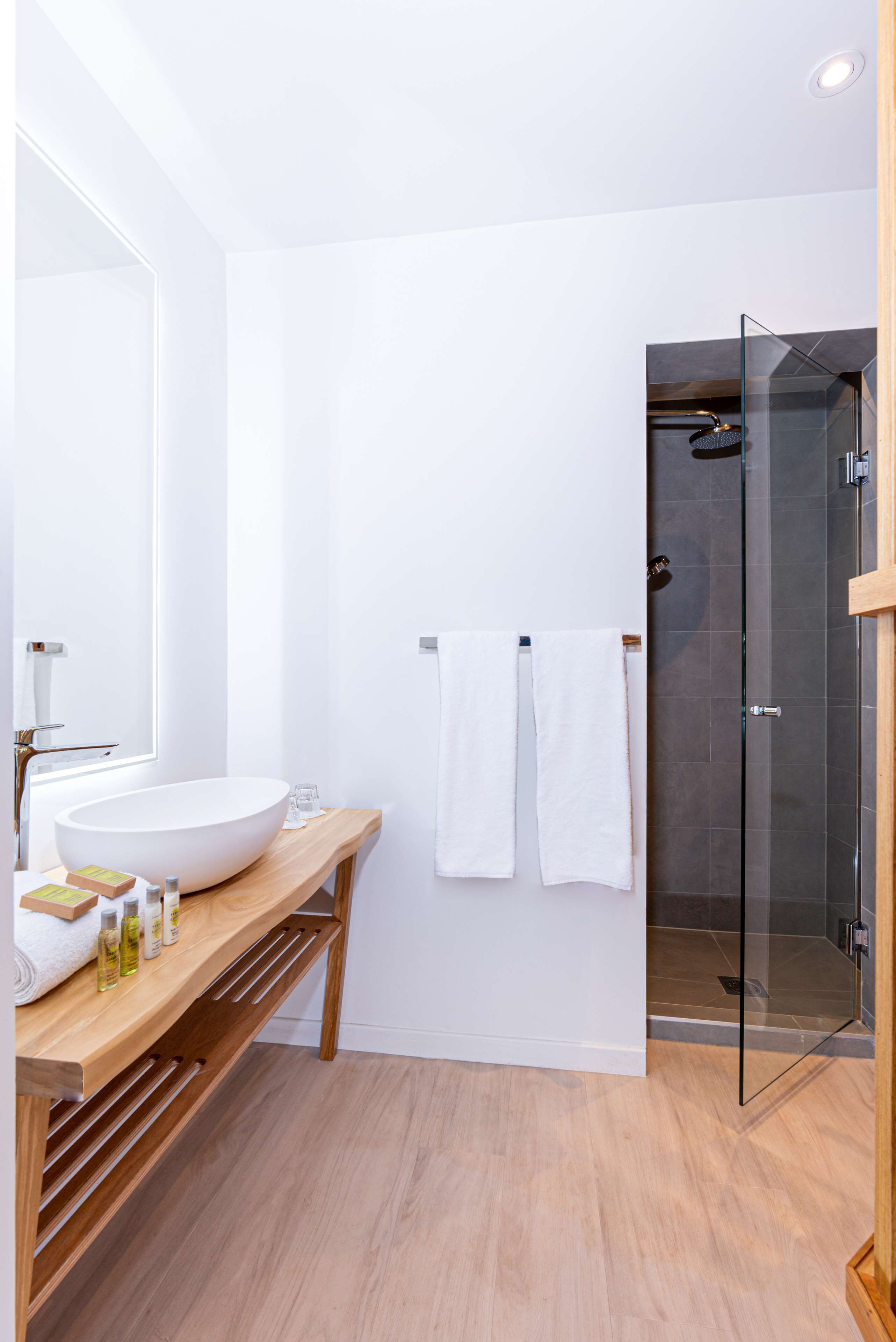 A modern bathroom with a large white sink, wooden vanity, and a glass shower enclosure.