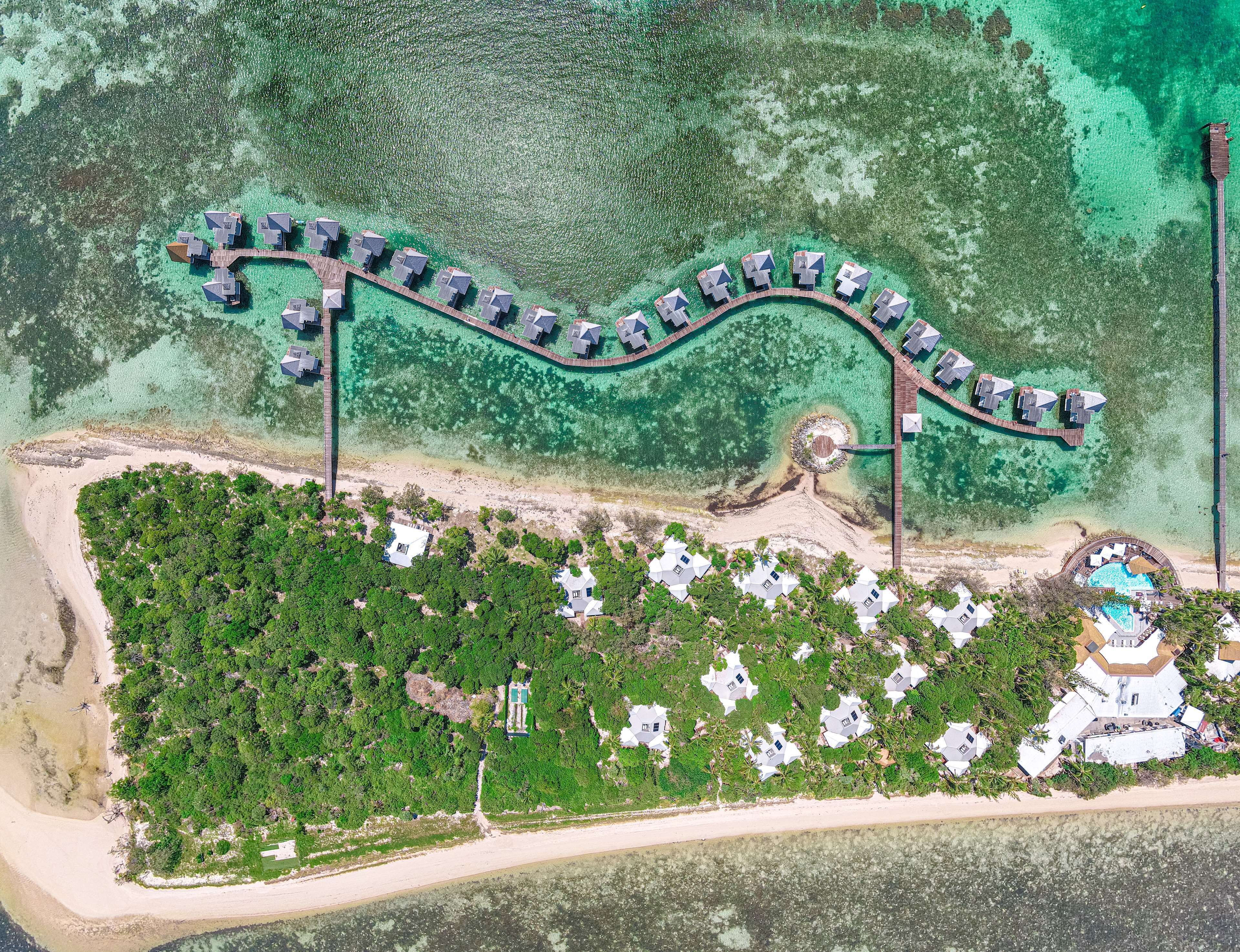 Vista aérea de un resort con un muelle largo, múltiples alojamientos tipo bungalow y una zona circular central con piscina.