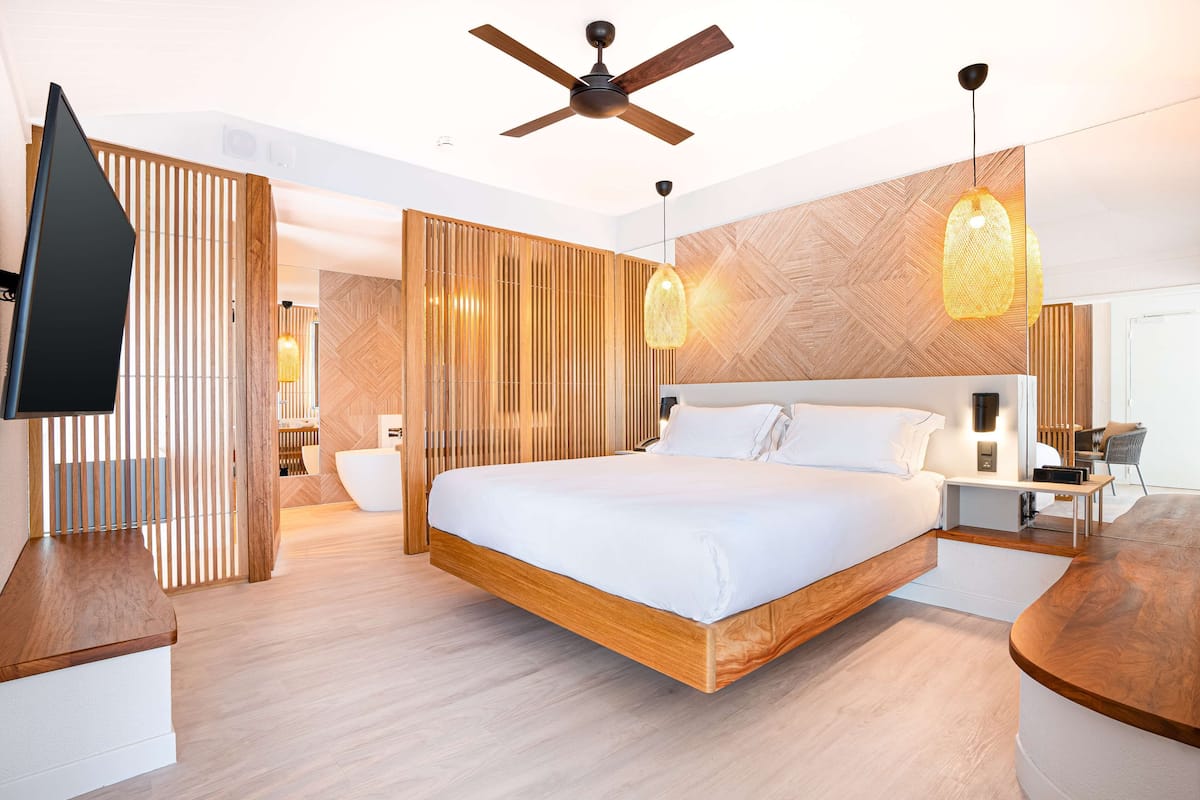 A modern bedroom with a large bed, wooden headboard, a ceiling fan, and pendant lighting.