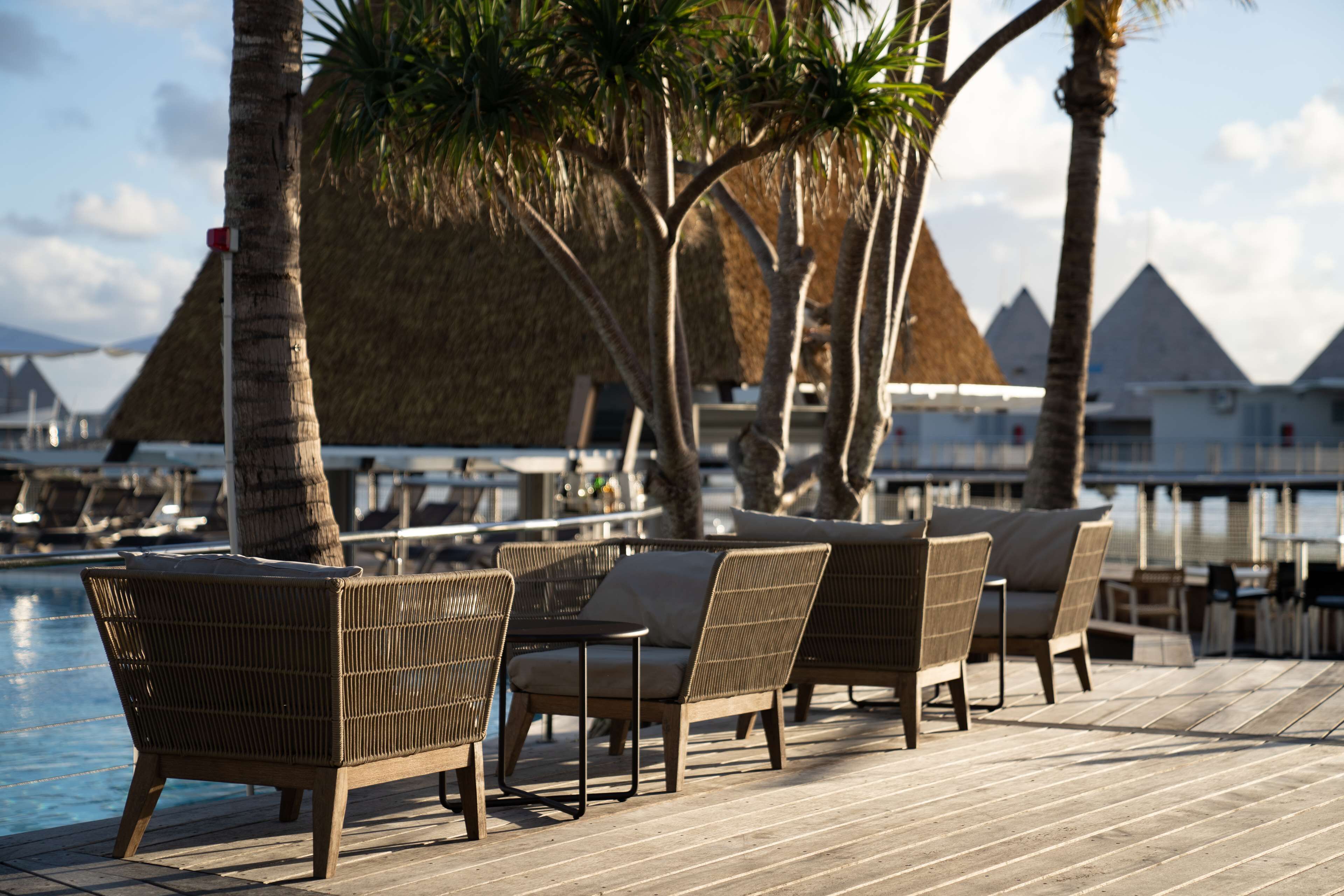 Terraza de madera con sillones de mimbre y piscina.