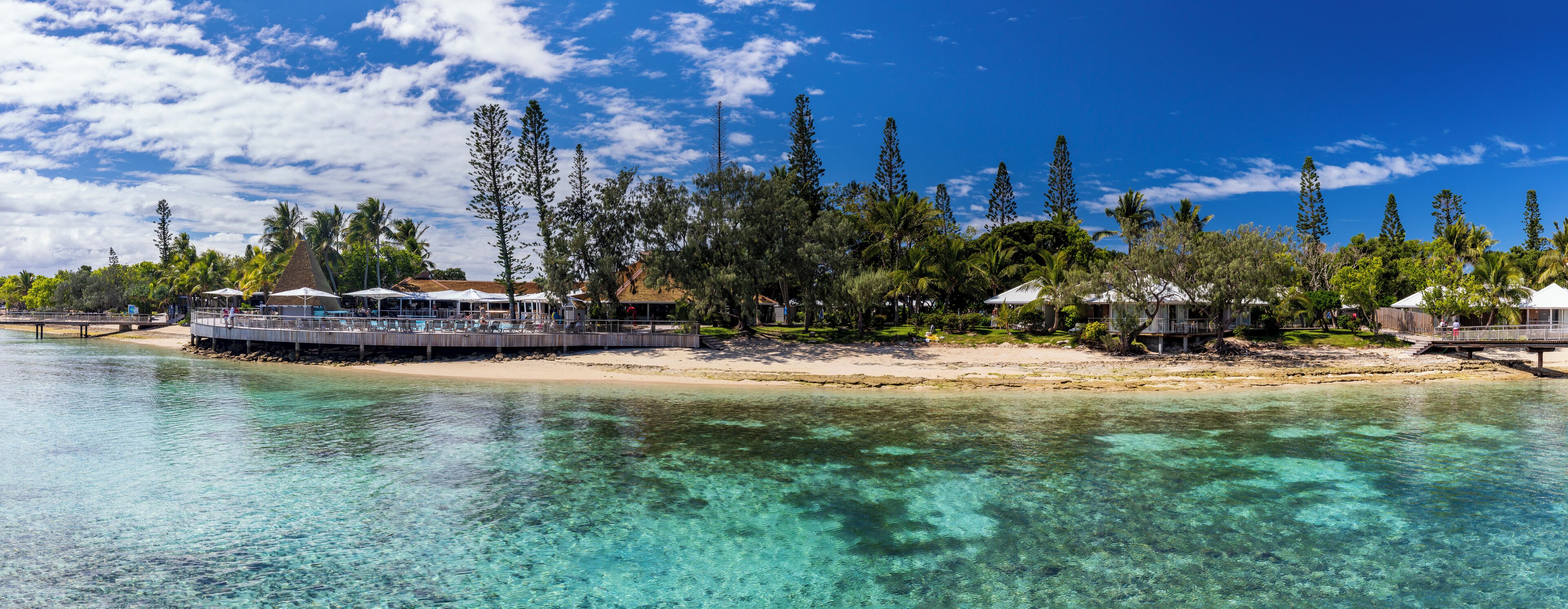 A beachfront resort with clear turquoise waters, a wooden pier, and several overwater bungalows.