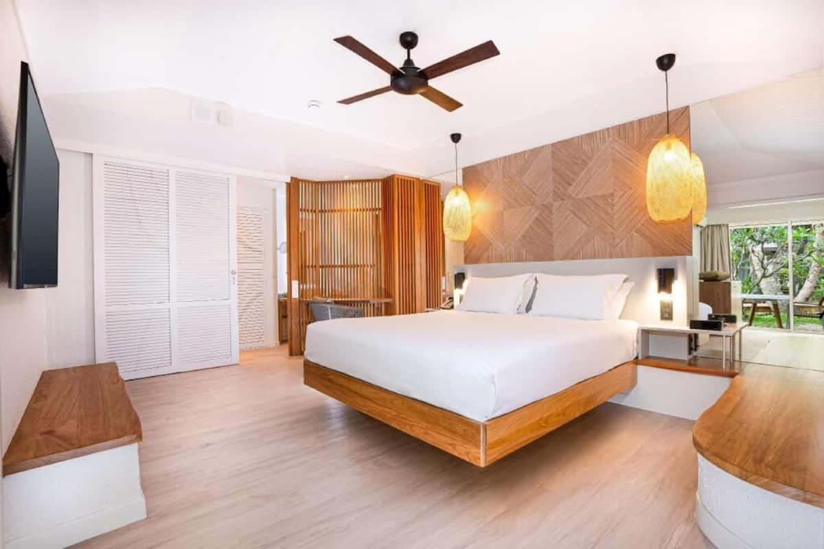 A modern bedroom with a bed, ceiling fan, wooden floor, and a TV mounted on the wall.