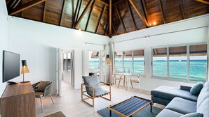 Amplia sala de estar con techo de madera, televisor, mesa de comedor y vista al océano.