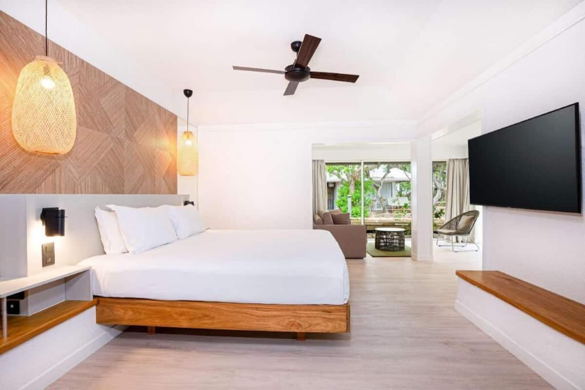 A modern bedroom with a bed, a ceiling fan, a TV, and a view of the outdoors.