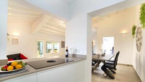 A modern kitchen with a central island, a dining area with a table and chairs, and a view of the outdoors.