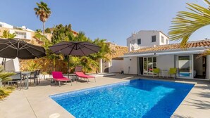A swimming pool with lounge chairs and umbrellas, surrounded by stone walls and palm trees.