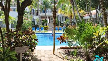A pool area with a pathway leading to a building, surrounded by tropical plants and palm trees.