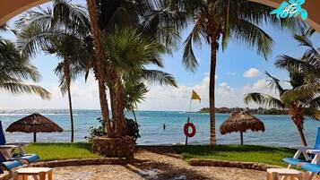A beach view with palm trees, a lifebuoy, and a thatched umbrella.