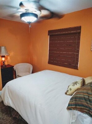 A bedroom with a bed, a chair, a nightstand, a lamp, and a window with a wooden blind. - Lakefront Casita (hot springs)