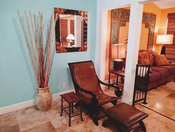 Un salon avec un fauteuil en cuir marron, une petite table en bois et un vase contenant des roseaux.