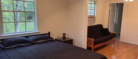 Un dormitorio con una cama grande, una mesita de noche, una silla y una ventana con vistas a árboles.