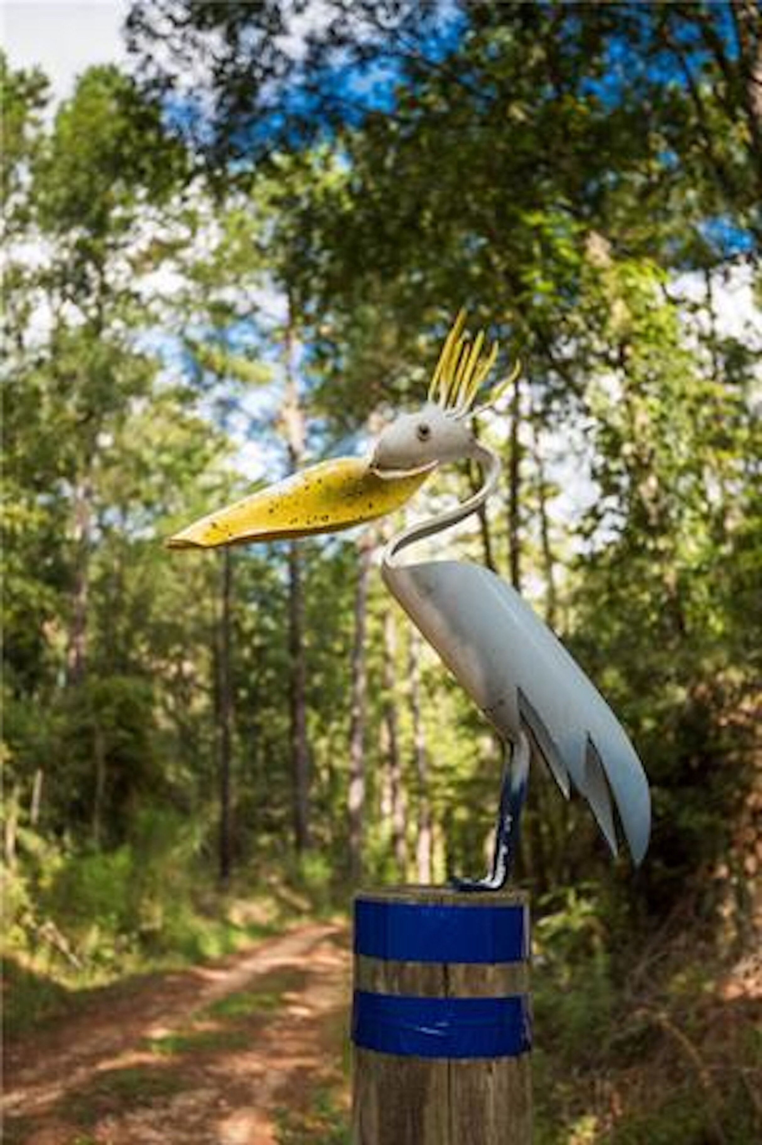 A bird sculpture on a wooden post in a forested area.