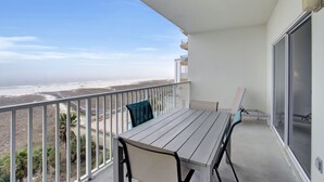 Een balkon met een tafel en stoelen, met uitzicht op een strand en een verafgelegen stadsbeeld.