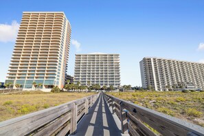 A wooden boardwalk leading to three high-rise buildings with balconies, under a clear sky. - Tidewater 408 by Liquid Life (Orange Beach)