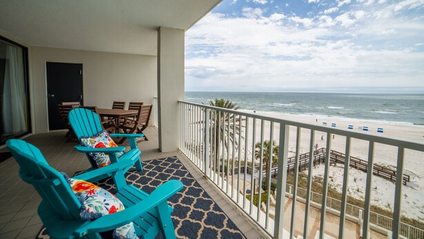 A balcony with turquoise chairs and a table, overlooking a beach with a railing and a view of the ocean. - Pelican Pointe 504 by Liquid Life (Orange Beach)