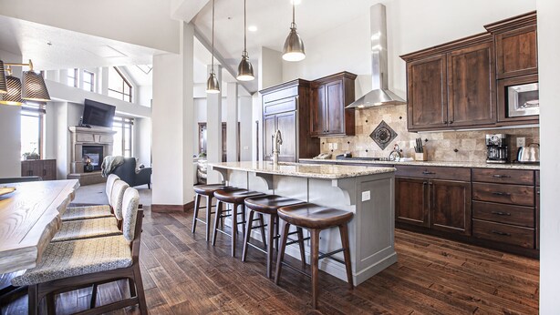 A spacious kitchen with a large island, dark wooden cabinets, and a stone backsplash. - Hyatt at the Canyons by Park City Vacations (Park City)