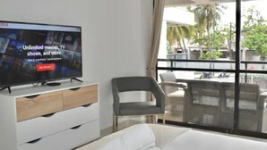 A hotel room with a bed, a TV displaying a movie service advertisement, a window with a view of palm trees, and a balcony with outdoor furniture. - Apartamento Vacacional San Andres (San Andrés)