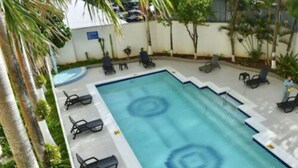 A rectangular swimming pool with a blue center and white edges, surrounded by lounge chairs and palm trees. - Apartamento Vacacional San Andres (San Andrés)