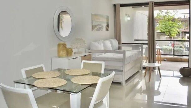 A modern living room with a glass dining table, white furniture, a sofa, and a large window offering a view of the outdoors. - Apartamento Vacacional San Andres (San Andrés)