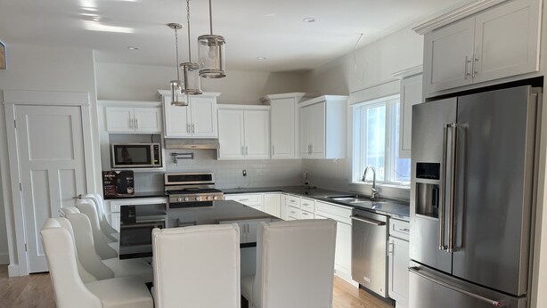 A modern kitchen with white cabinetry, stainless steel appliances, and a central island with bar stools.
