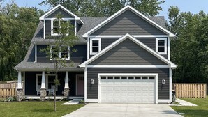 A two-story house with a garage, a front porch, and a stone foundation.