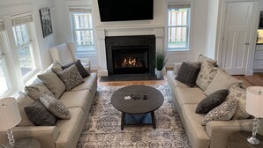 A living room with a fireplace, two sofas, a coffee table, and a TV mounted above the fireplace.