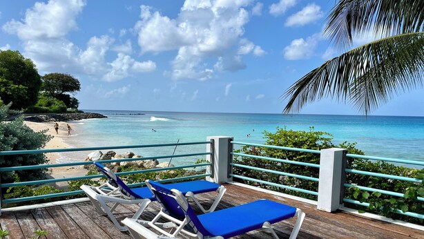 Een houten terras met twee blauwe lounge fauteuils en een balustrade met uitzicht op het strand.