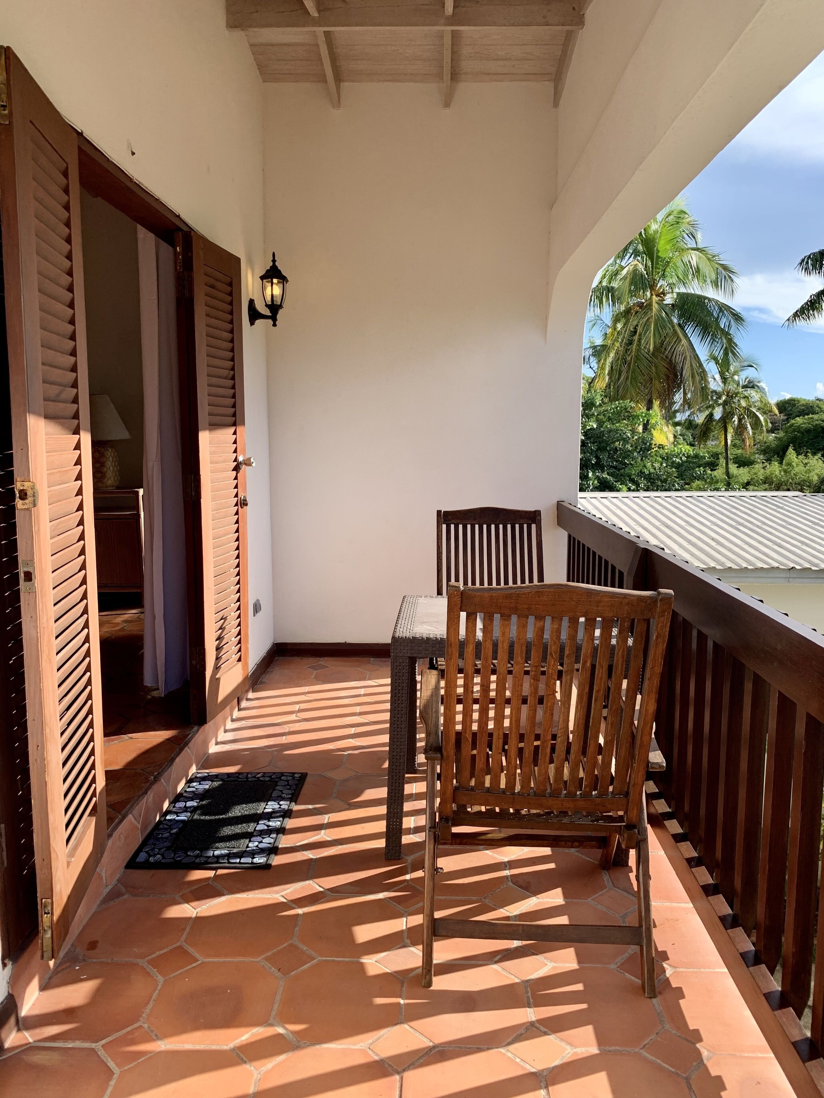 Un balcon avec une chaise et une table en bois, un sol carrelé et une vue sur des palmiers.