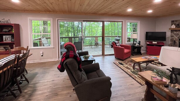 A spacious living room with a wooden ceiling, large windows, a dining area, and a television.