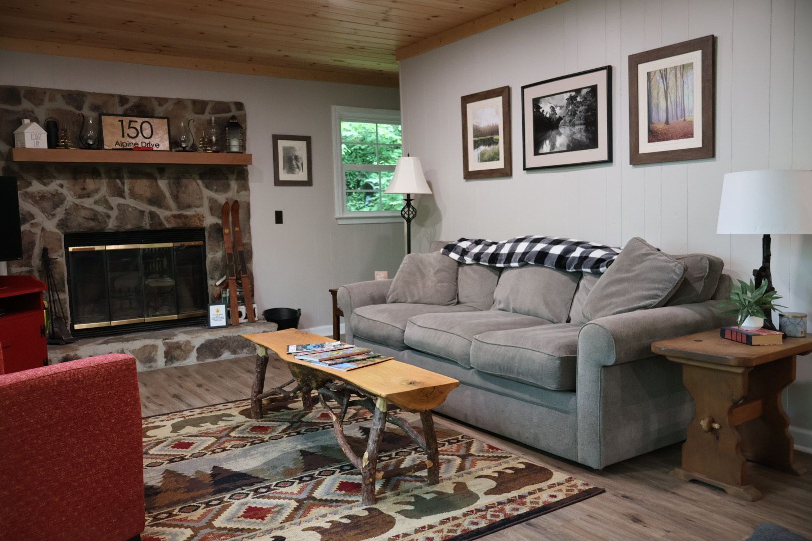 A cozy living room with a stone fireplace, a grey sofa, a wooden table, and a red armchair.