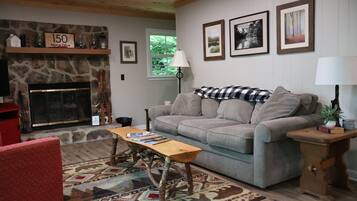 A cozy living room with a stone fireplace, a grey sofa, a wooden table, and a red armchair.