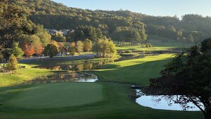 A golf course with a pond, surrounded by trees and hills.