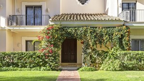 A well-maintained garden with a stone pathway leading to a building with a tiled roof and a dark wooden door. - Penthouse in Andalucía del Mar for 4 people | ADM 2-403 (Puerto Banús - Marbella)