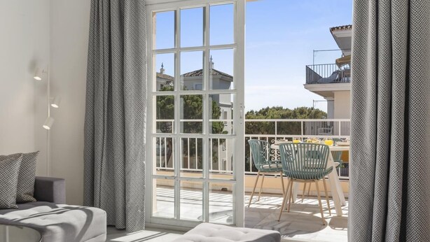 A modern living room with a sofa, a small table, and a balcony with outdoor seating. - Penthouse in Andalucía del Mar for 4 people | ADM 2-403 (Puerto Banús - Marbella)