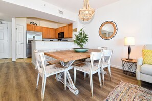 Uma sala de jantar com uma mesa de madeira e cadeiras brancas, um lustre, um espelho e um abajur.