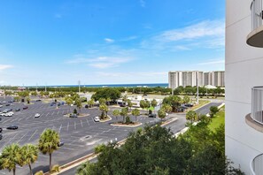 A parking lot with multiple cars, palm trees, and a view of high-rise buildings in the background. - Fully Updated! Beautiful 2 Bedroom Condo with Seasonal Beach Shuttle! (Destin)