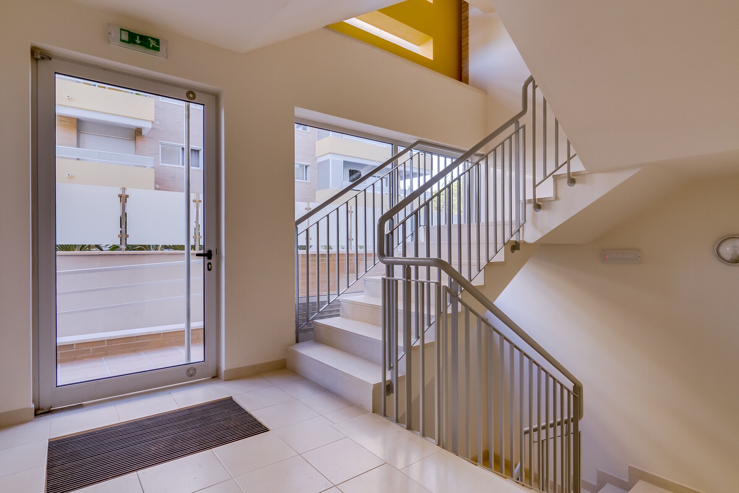 Ein moderner Hotelzugang mit Glastür, einer Metalltreppe und Blick auf die Straße.