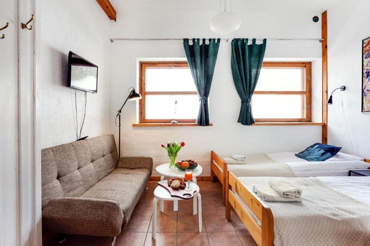 Una habitación acogedora con un sofá, una mesita con un florero, una cama y un televisor montado en la pared.