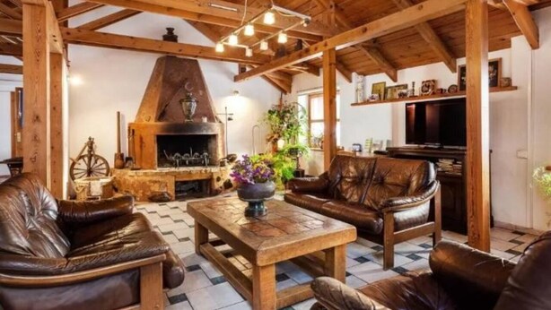 A rustic interior with exposed wooden beams, a stone fireplace, leather sofas, and a wooden coffee table. - B and B Saules Namai (Vilnius)