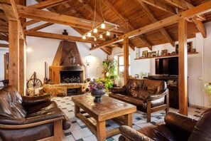 Un intérieur rustique avec des poutres apparentes, une cheminée en pierre, des canapés en cuir et une table basse en bois.