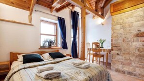 A cozy bedroom with a wooden bed, a small table with chairs, a window with curtains, and a stone wall. - B and B Saules Namai (Vilnius)