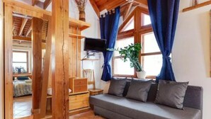 A cozy room with a sofa, wooden beams, a TV, and a plant. - B and B Saules Namai (Vilnius)