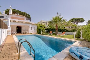 A swimming pool with a clear blue water, surrounded by a patio area with lounge chairs and a palm tree.