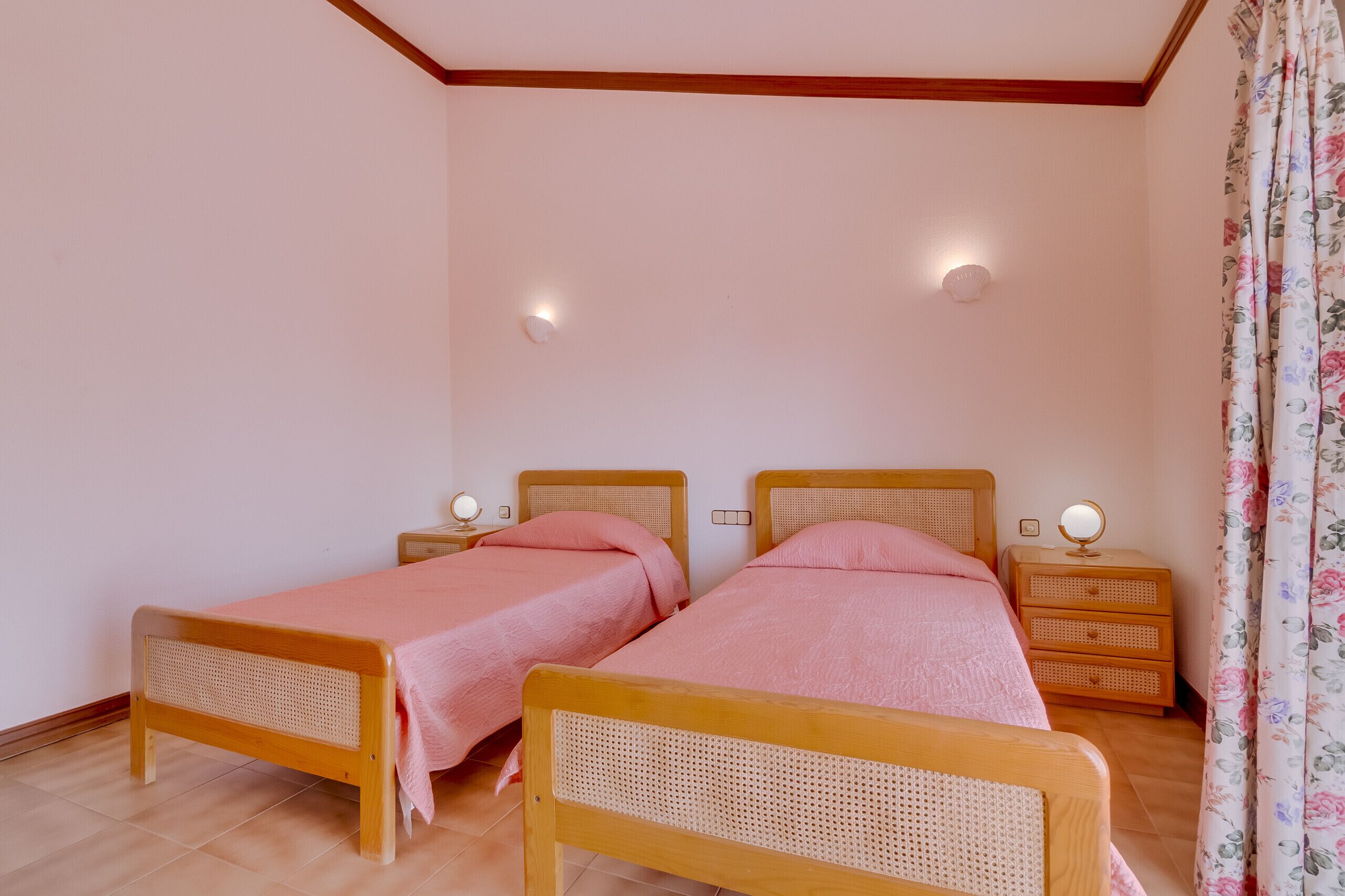A bedroom with two wooden beds, each with a headboard and footboard, and a bedside table with a mirror.