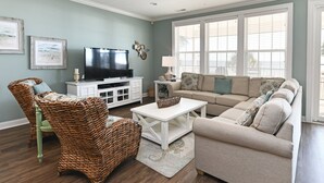 A living room with a television, wicker chair, sofa, and a white coffee table. - Oceanfront 5 BR Beach House with a Private Pool! Tranquility (Surfside Beach)