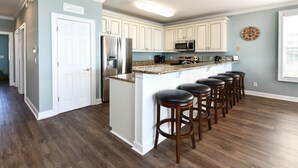 A kitchen with white cabinets, a stainless steel refrigerator, a microwave, and a granite countertop. - Oceanfront 5 BR Beach House with a Private Pool! Tranquility (Surfside Beach)